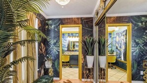 A room with a large mirror, a desk, and a chair. There are potted plants and a leopard print rug on the floor.