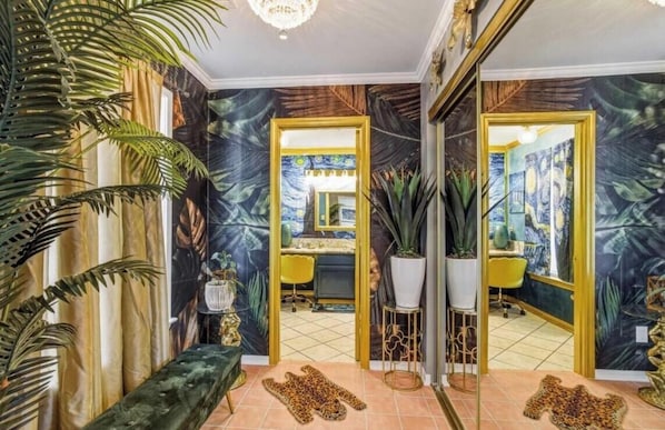 Una habitación con un espejo grande, un escritorio y una silla. Hay plantas en macetas y una alfombra de estampado de leopardo en el suelo.