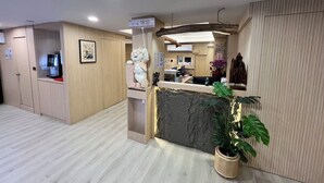 Un espace d’accueil comprenant un comptoir de réception en bois, une grande plante en pot et un présentoir avec un ordinateur.