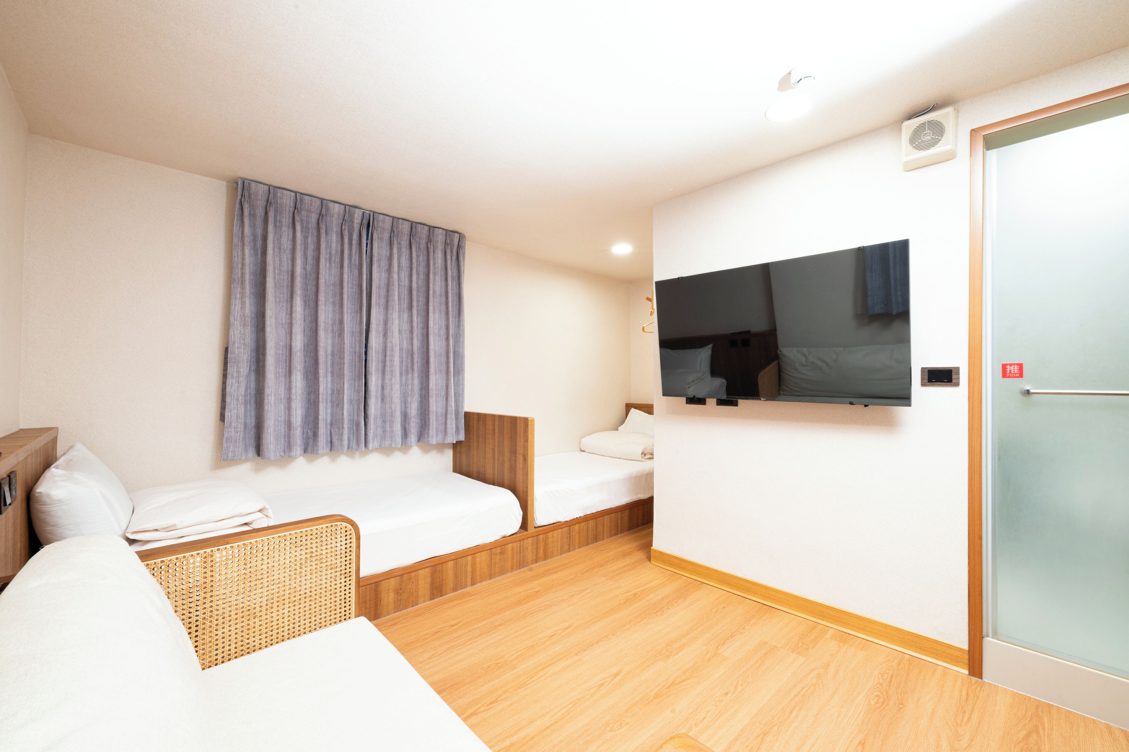 A hotel room with a single bed, a sofa, a television mounted on the wall, and a sliding door.
