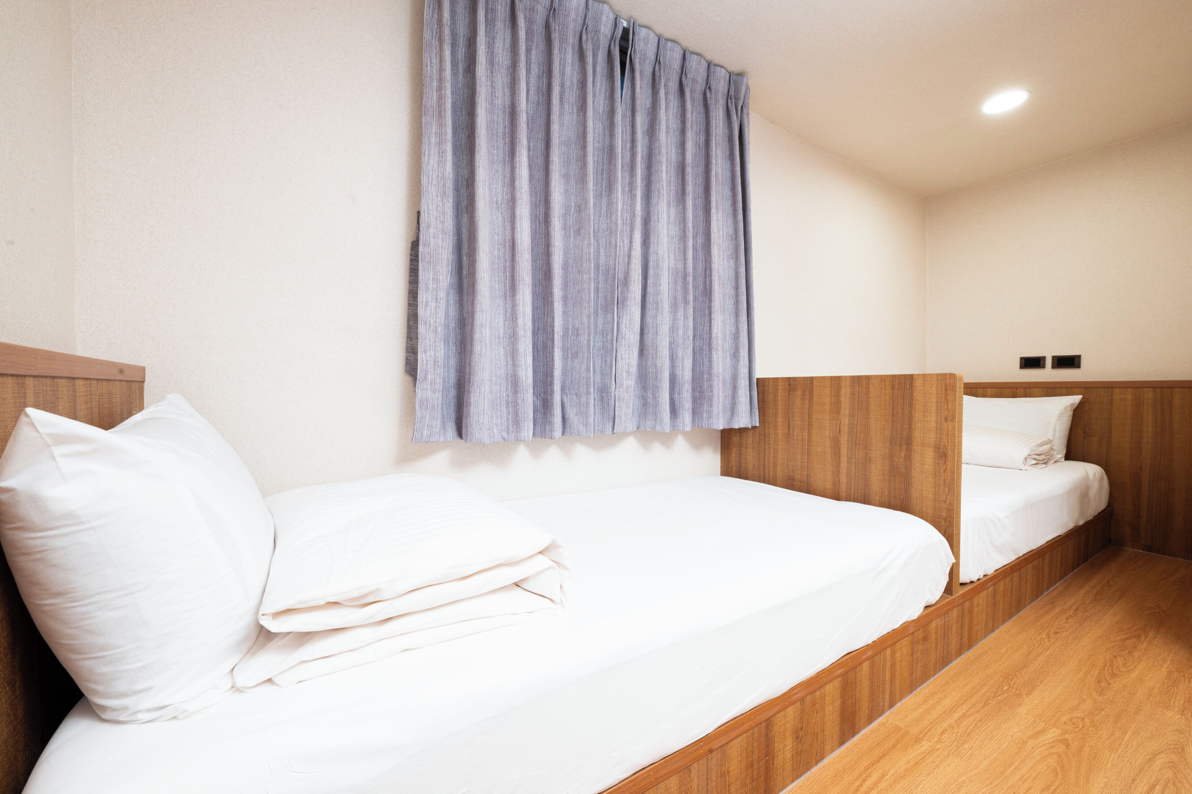 A hotel room with two single beds, wooden headboards, and a light-colored wall.