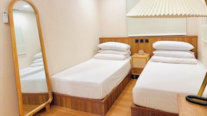 Une chambre d’hôtel avec deux lits simples, une tête de lit en bois, une table de chevet avec une lampe, un miroir et un appareil de climatisation.