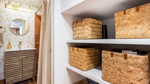 Un baño con tocador de madera, espejo y estantes con cestas tejidas.