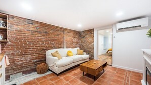 Una sala de estar con un sofá blanco, una mesa de centro de madera y una pared de ladrillo.