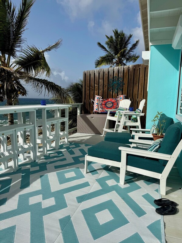 Un patio con mobiliario blanco, piso estampado y vista al océano.