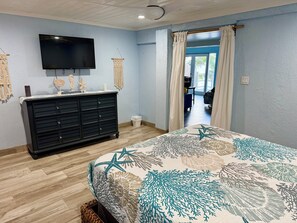 Un dormitorio con cama, cómoda, televisor y vistas al exterior.