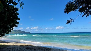 Una playa con aguas turquesas cristalinas, una orilla arenosa y una montaña al fondo.