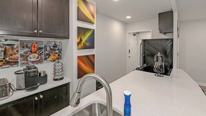 Une cuisine moderne avec des meubles de couleur sombre, un plan de travail blanc, un évier en acier inoxydable, une machine à café, une bouilloire et un réfrigérateur.