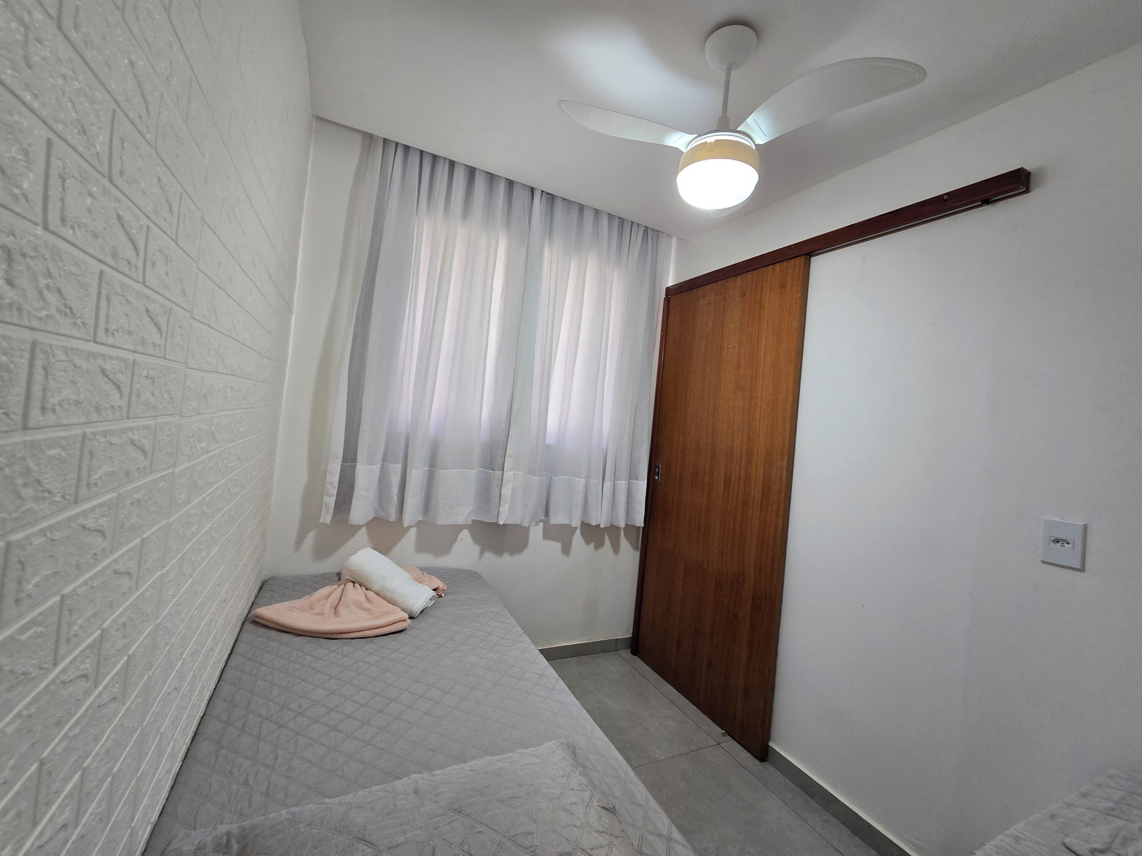 A room with a white brick wall, a wooden door, a ceiling fan, and a window with sheer curtains.