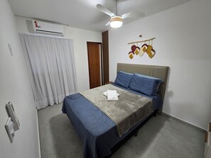 A bedroom with a bed, a ceiling fan, an air conditioning unit, a door, and a wall decoration. - A cozy house just 40 steps from the ocean. (Marataízes)