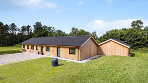 Un bâtiment moderne en bois, doté d’un toit en pente, d’une allée en gravier et d’une zone herbeuse.