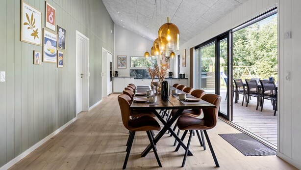 Un espace de salle à manger moderne, avec une longue table, des chaises marron et un luminaire suspendu original.