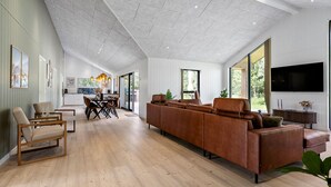 Un vaste espace de vie doté d’un haut plafond, d’un grand canapé, d’une table à manger avec des chaises et d’un téléviseur fixé au mur.