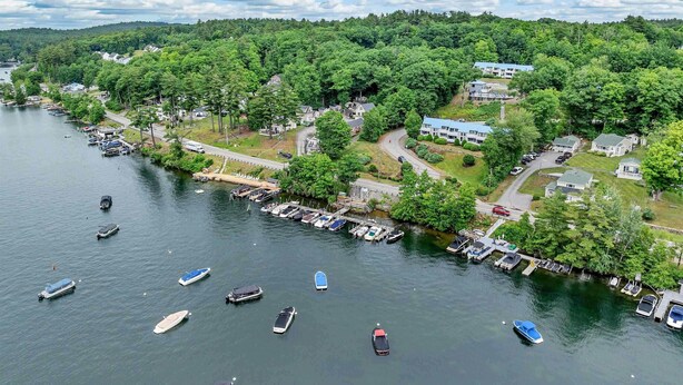 Une propriété au bord du lac, avec des bateaux amarrés, une route menant aux bâtiments et une colline boisée en arrière-plan.