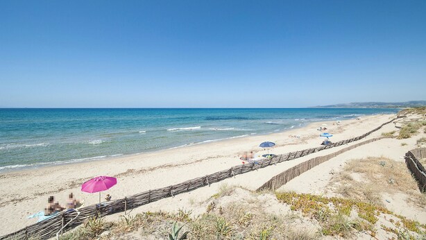 A beach with a clear sky, a sandy shore, and a stone wall running parallel to the beach. - Stunning home in Castelsardo with WiFi (Castelsardo)