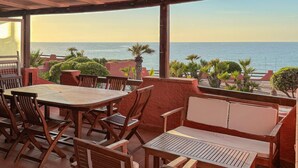 A covered outdoor seating area with wooden tables and chairs, overlooking a body of water. - Stunning home in Castelsardo with WiFi (Castelsardo)