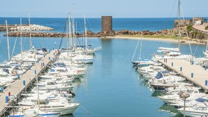 A marina with numerous boats docked, a sandy beach, and a rocky structure in the background. - Stunning home in Castelsardo with WiFi (Castelsardo)