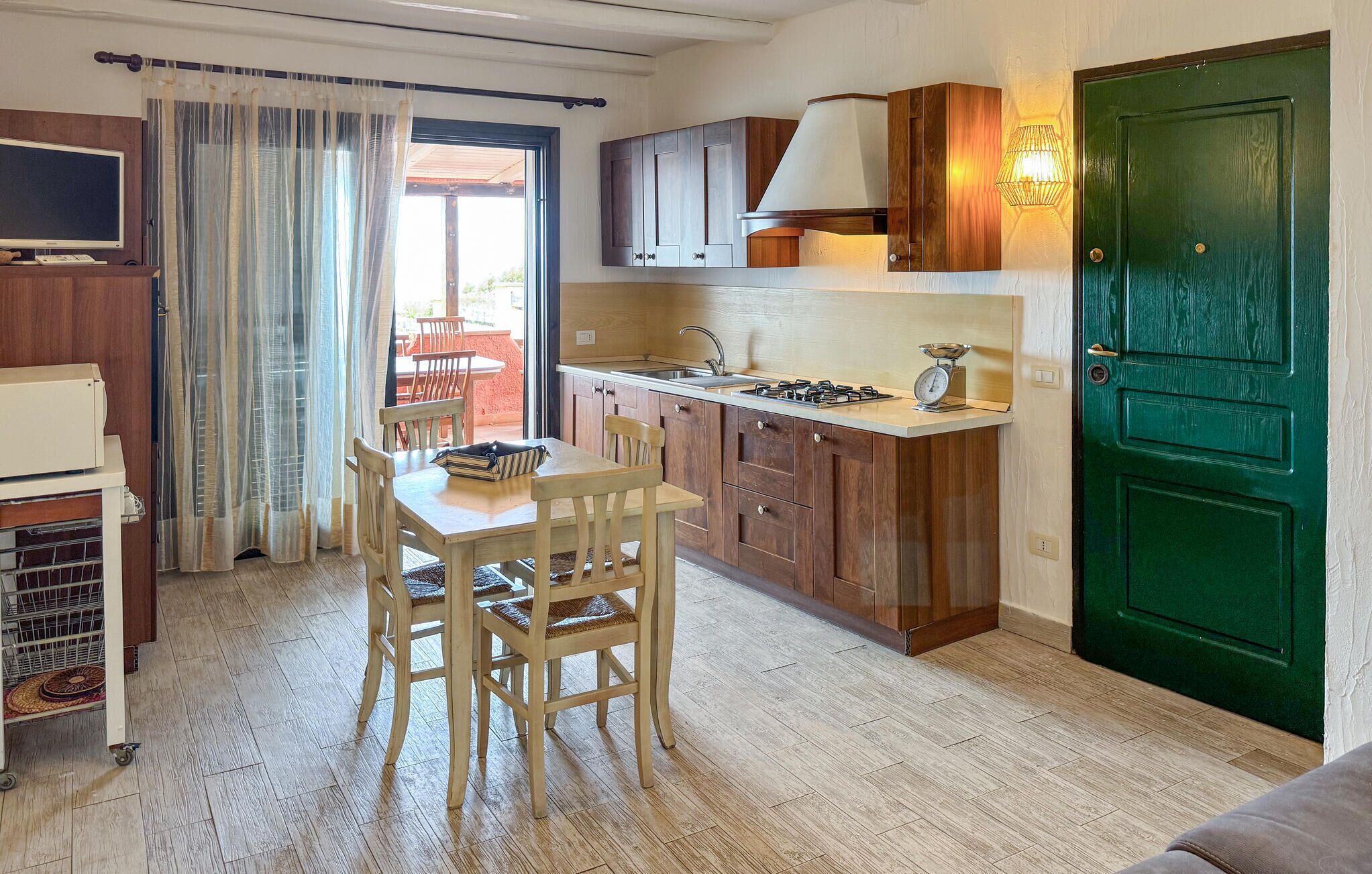 Una cucina compatta con mobili in legno, un'area pranzo con tavolo e sedie, e una porta verde.
