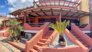 A building with a curved roof, a staircase leading to a balcony, and a small garden area with palm plants. - Stunning home in Castelsardo with WiFi (Castelsardo)