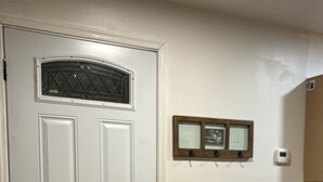 Een witte deur met een raam, een klein plankje met twee foto's, een thermostaat aan de muur en een potplant.