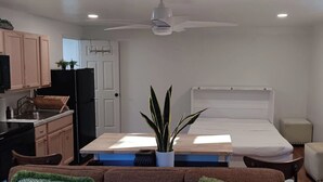 Een compacte kamer met een bed, kitchenette en plafondventilator.