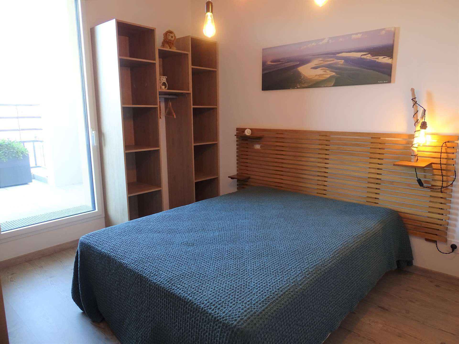 Une chambre à coucher avec un lit, une tête de lit en bois, des étagères intégrées, un tableau et une fenêtre.
