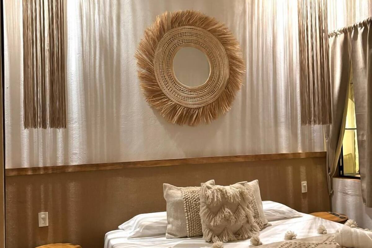 A bedroom with a large bed, a round mirror, and two hanging light fixtures.