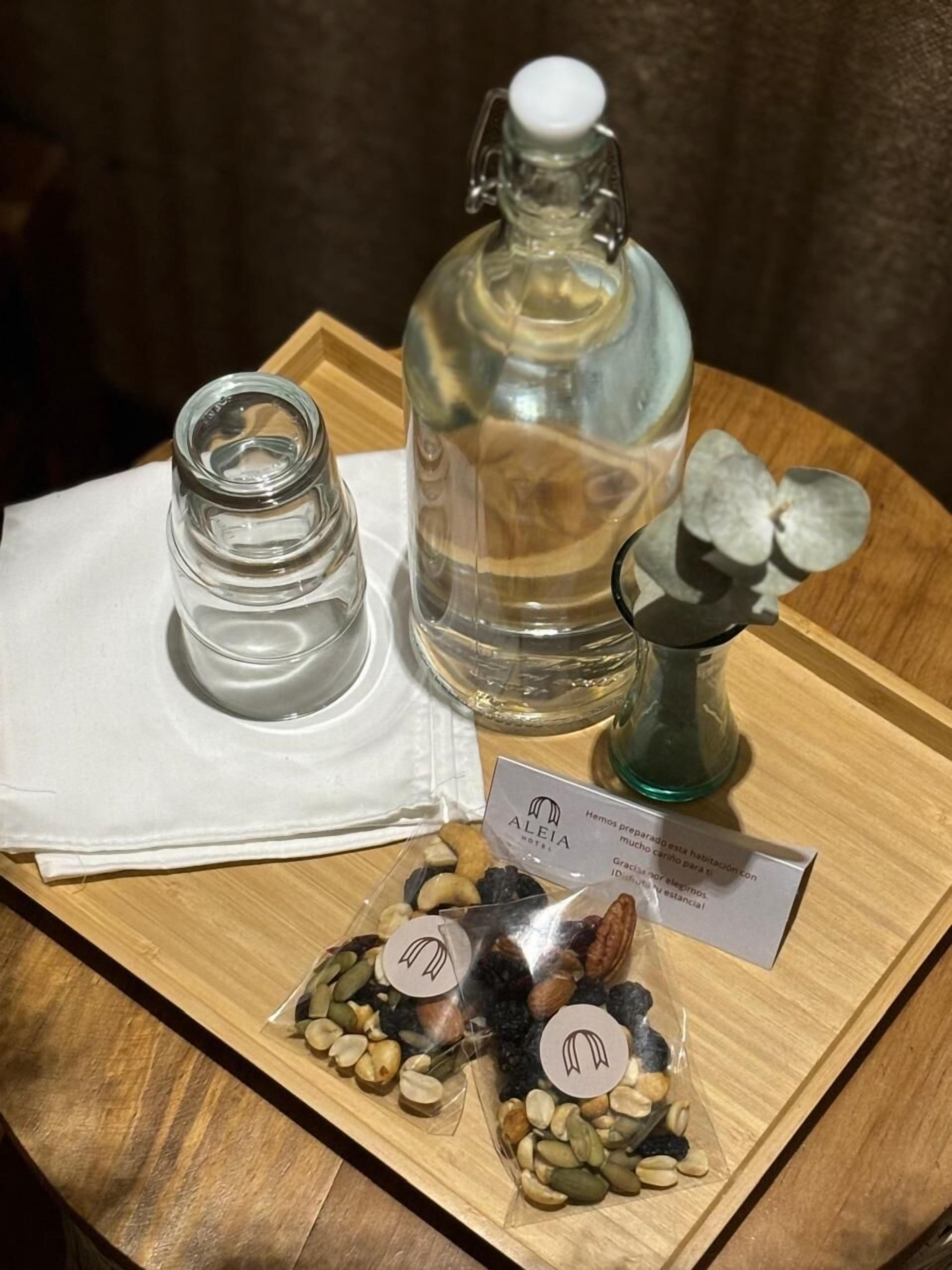Una bandeja de madera con una botella de vidrio, un recipiente de vidrio más pequeño y dos bolsas de nueces.