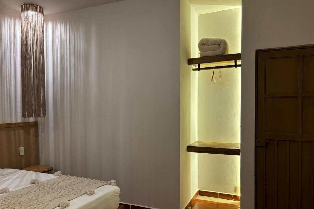 A bedroom with a bed, a bedside table, a hanging light fixture, and a built-in shelf with a towel.