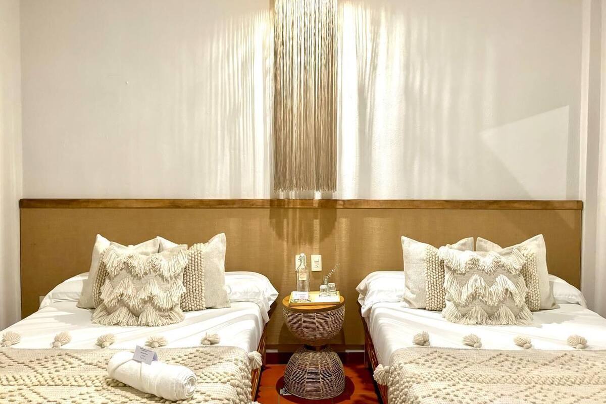 A hotel room with two beds, a chandelier, and a round table with a bottle and glass.