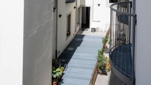 A narrow corridor between two white buildings with balconies, a small outdoor area with plants, and a clear sky. - City Gallery Apartments (Trieste)