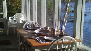 Mesa de comedor dispuesta con platos, tazas y cubiertos, con vista a un cuerpo de agua.