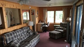 Interior acogedor de una cabaña con un sofá a cuadros, una mesita, una silla y un televisor.