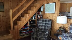 Un interior de madera con una escalera, un sillón a cuadros, una estantería y un mapa en la pared.