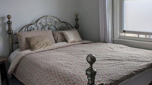 Una cama con colcha estampada de flores, cabecera con diseño decorativo y ventana con cortinas.