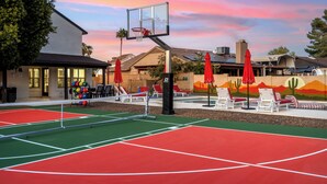An outdoor tennis court with a net, red and green playing areas, and red umbrellas. - Cobo Escape | Heated Pool | MiniGolf | Game Room (Scottsdale)