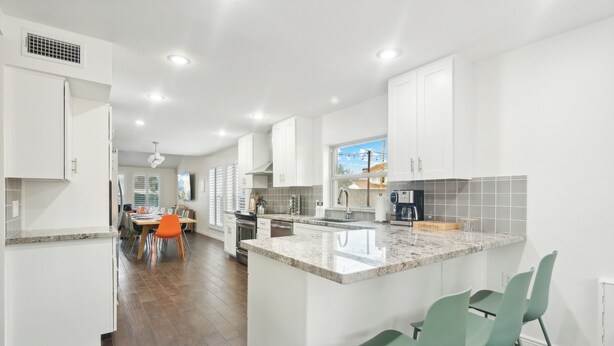 A modern kitchen with white cabinets, a granite countertop, and a dining area with orange chairs. - Cobo Escape | Heated Pool | MiniGolf | Game Room (Scottsdale)