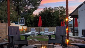 A patio area with Adirondack chairs, a fire pit, and red umbrellas. - Cobo Escape | Heated Pool | MiniGolf | Game Room (Scottsdale)