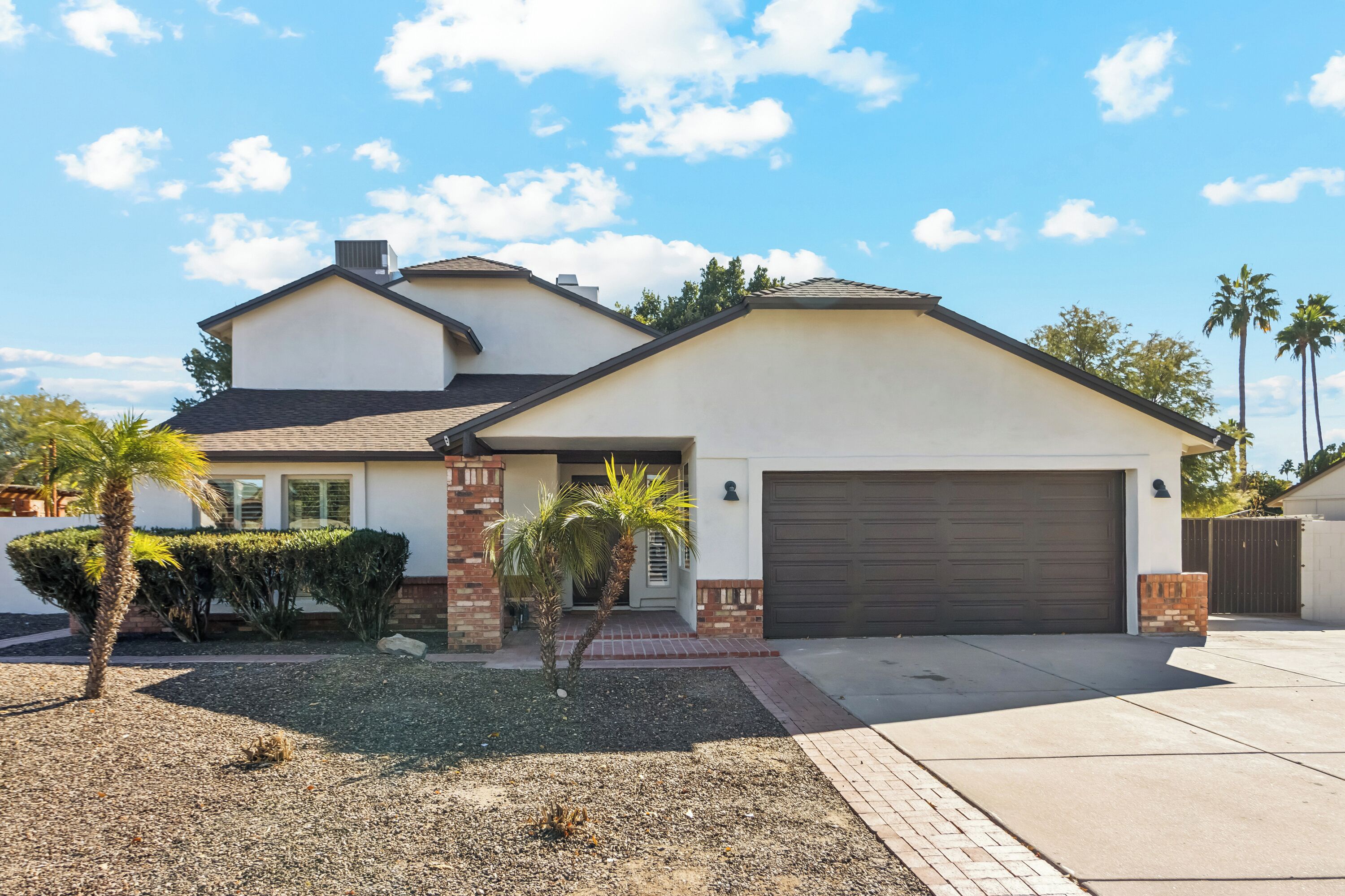 A single-story house with a garage, a small front yard with palm trees, and a clear sky.