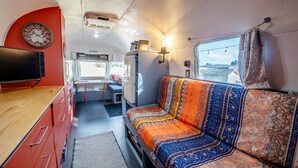Interior compacto de autocaravana con kitchenette, sofá cama, un reloj y ventana con vistas.