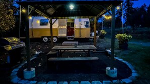 Un área de picnic techada con mesa y bancos, una parrilla y una caravana estacionada cerca.