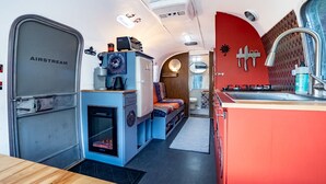 Cocina moderna y compacta con una pared de acento roja, un espacio de descanso pequeño y una puerta de remolque Airstream visible.