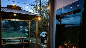 Un patio exterior con una mesa y sillas de madera, una parrilla y una chimenea a la vista a través de un muro de cristal.