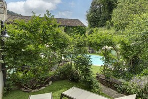 Un jardin luxuriant avec une piscine, des murs en pierre et une cloche.