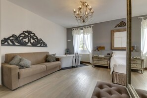 Une chambre à coucher avec un canapé, un lit, un miroir, un lustre et une fenêtre avec des rideaux.