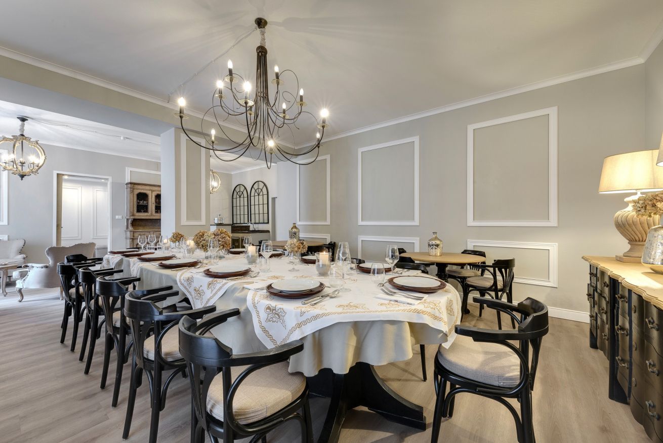 Ein formeller Speisesaal mit einem großen Esstisch, gedeckt für eine Mahlzeit, umgeben von Stühlen und einer darüber hängenden Chandelierleuchtre.