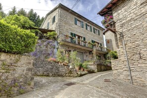 A stone building with a balcony, surrounded by greenery and potted plants. - MyExclusiveItaly - Entire Hilltop Villa with Private Pool (Palazzuolo Sul Senio)