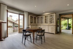 Une pièce spacieuse avec une table et des chaises en bois, une grande armoire aux portes vitrées et un balcon offrant une vue sur l’extérieur.