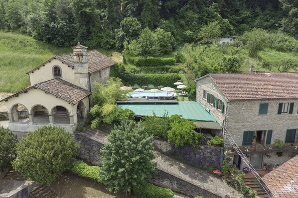Un bâtiment traditionnel en pierre, doté d’un clocher, d’une petite cour avec une piscine et d’une végétation luxuriante qui entoure la propriété.