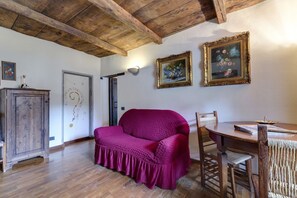 A room with wooden beams, a wooden cabinet, a purple sofa, a dining table with chairs, and two framed paintings on the wall. - MyExclusiveItaly - Entire Hilltop Villa with Private Pool (Palazzuolo Sul Senio)